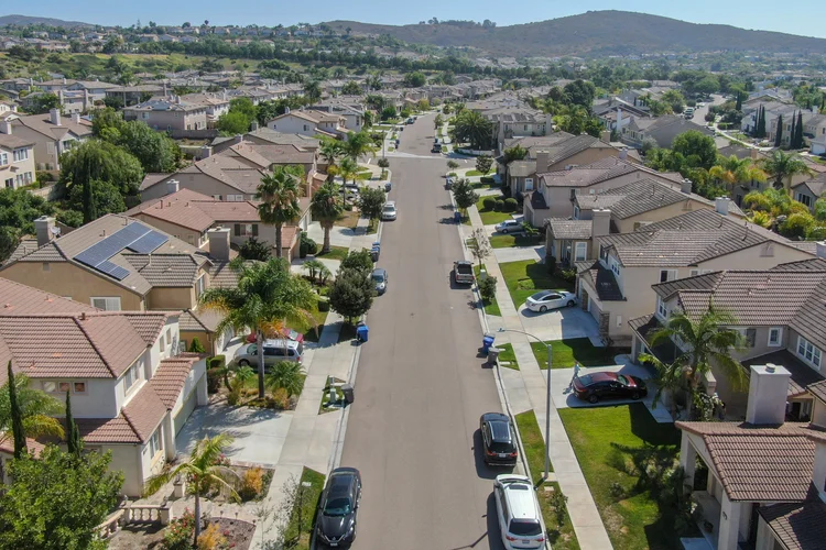 Aerial view of a sunny residential street lined with two-story homes and landscaped yards.